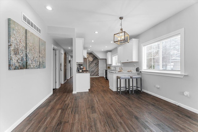 kitchen featuring dark wood-type flooring, hanging light fixtures, a kitchen breakfast bar, kitchen peninsula, and white cabinets