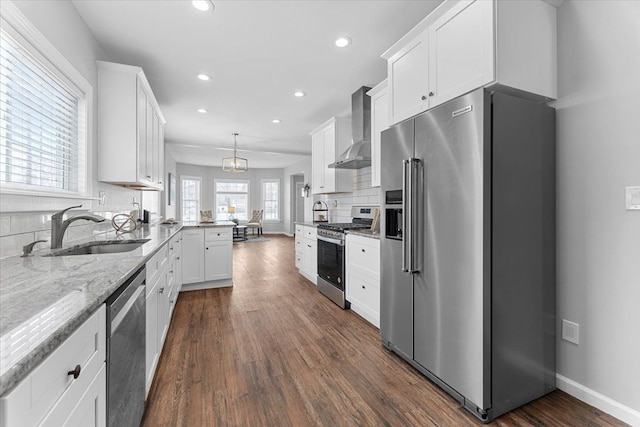 kitchen featuring appliances with stainless steel finishes, decorative light fixtures, sink, white cabinets, and wall chimney range hood