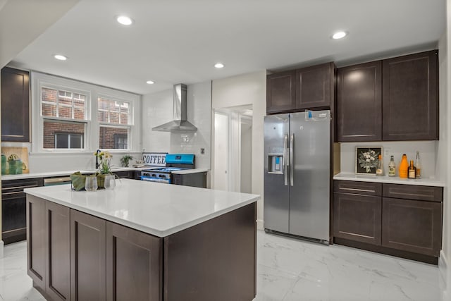 kitchen with dark brown cabinetry, a center island, wall chimney exhaust hood, stainless steel appliances, and backsplash