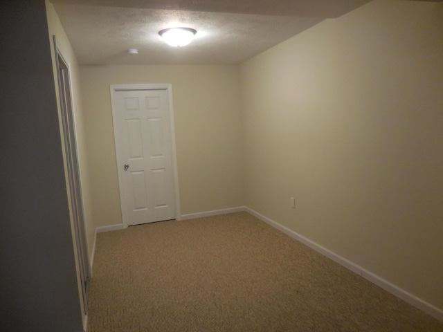 empty room with light carpet, a textured ceiling, and baseboards