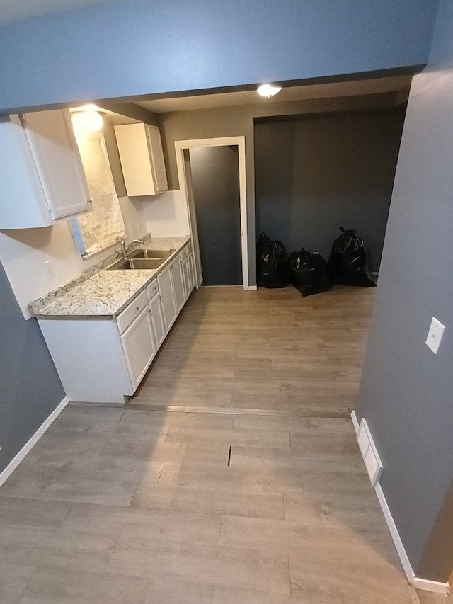 kitchen featuring light stone counters, white cabinetry, and sink