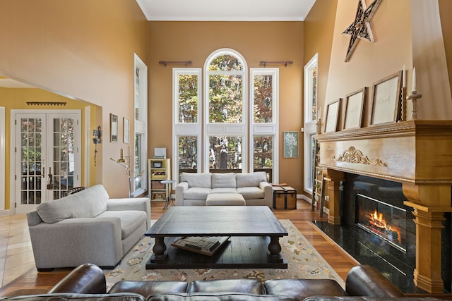 living room featuring a high end fireplace, french doors, light wood-type flooring, ornamental molding, and a high ceiling