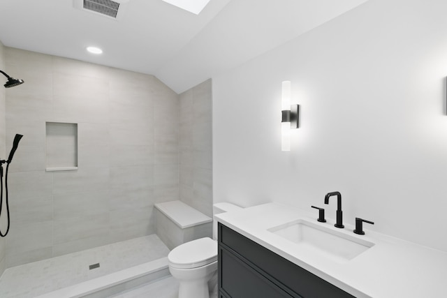 bathroom featuring tiled shower, a skylight, vanity, and toilet