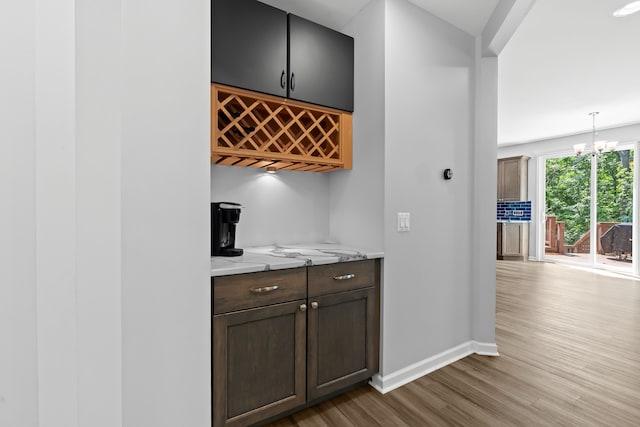 bar featuring light stone countertops, dark brown cabinets, decorative light fixtures, light hardwood / wood-style flooring, and a chandelier