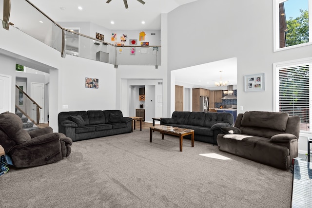 carpeted living room with a towering ceiling and ceiling fan with notable chandelier