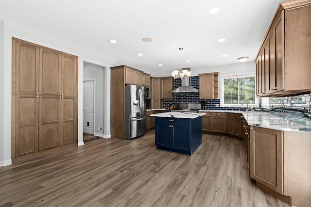 kitchen with a center island, hanging light fixtures, wall chimney range hood, stainless steel fridge with ice dispenser, and hardwood / wood-style floors