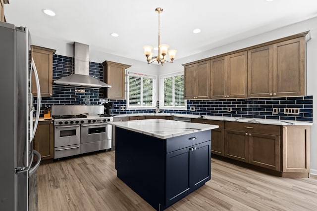 kitchen with a center island, wall chimney exhaust hood, stainless steel appliances, pendant lighting, and light hardwood / wood-style floors