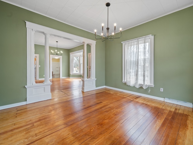 unfurnished room featuring decorative columns, ornamental molding, wood-type flooring, and an inviting chandelier