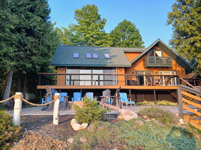 rear view of property with a wooden deck, a patio, a balcony, and a shingled roof