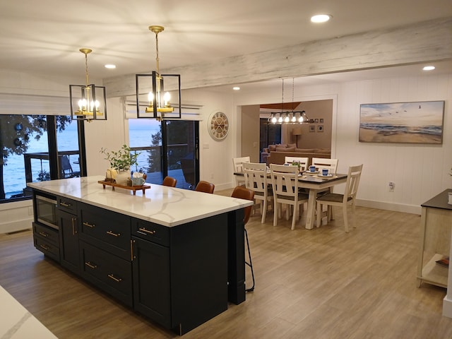 kitchen featuring light wood-type flooring, beam ceiling, stainless steel microwave, dark cabinetry, and a center island