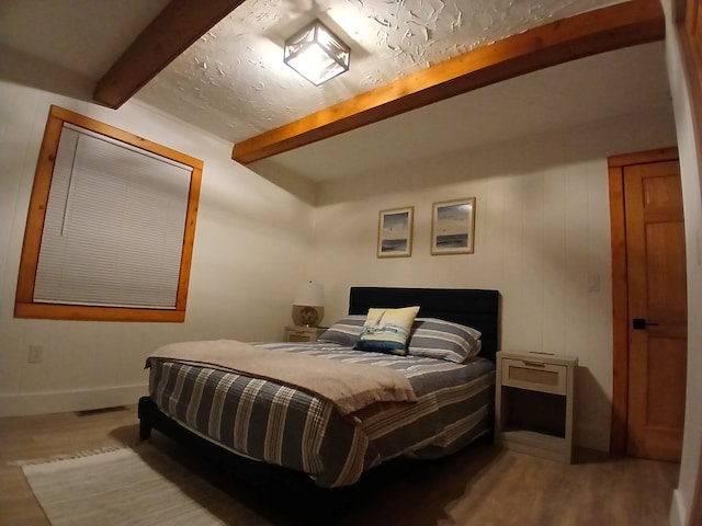 bedroom featuring beamed ceiling, baseboards, visible vents, and wood finished floors