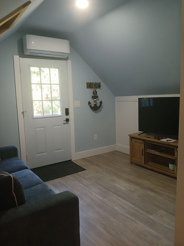 interior space with vaulted ceiling, a wall mounted AC, baseboards, and wood finished floors