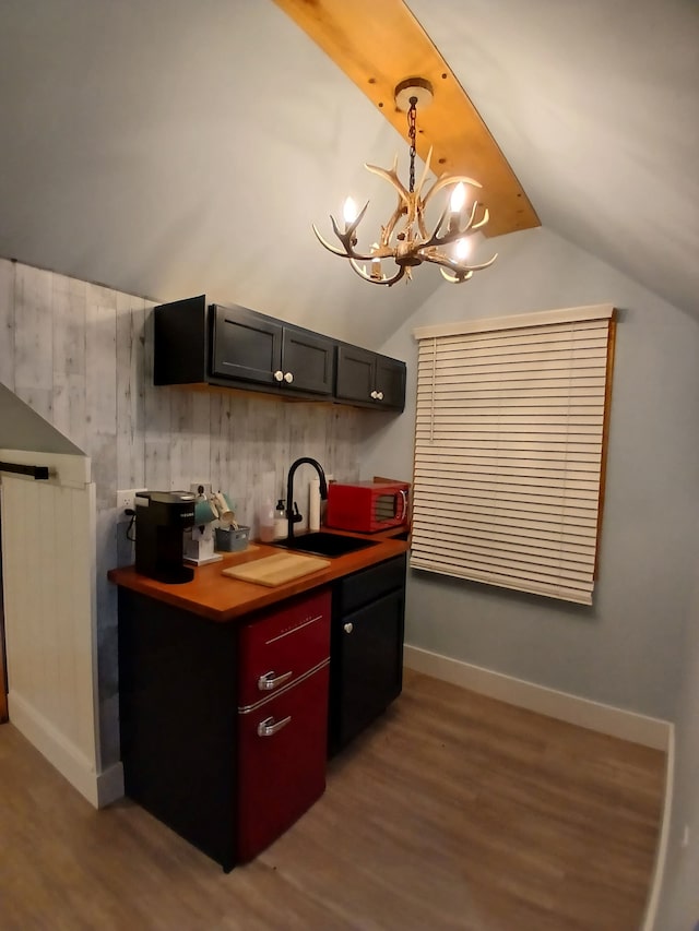 kitchen featuring baseboards, light wood-style flooring, a sink, vaulted ceiling, and a chandelier