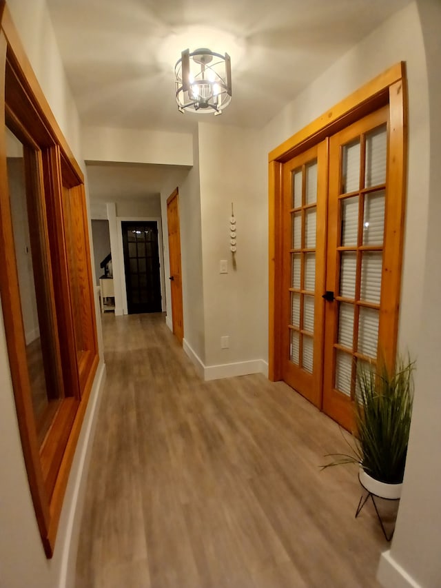 corridor featuring french doors, baseboards, and wood finished floors