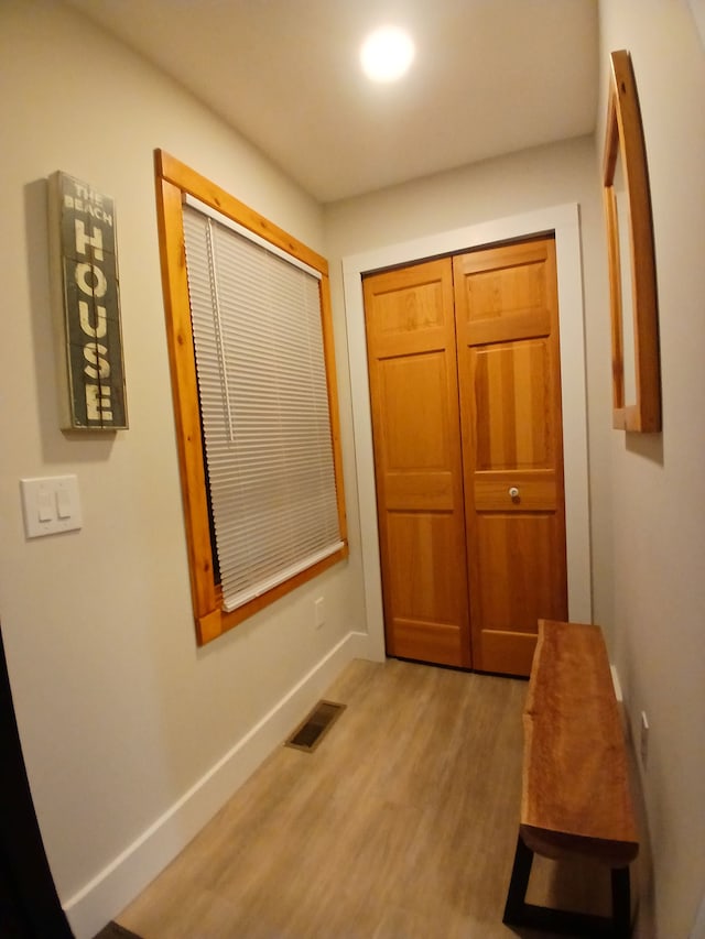 hall featuring baseboards, visible vents, and light wood finished floors