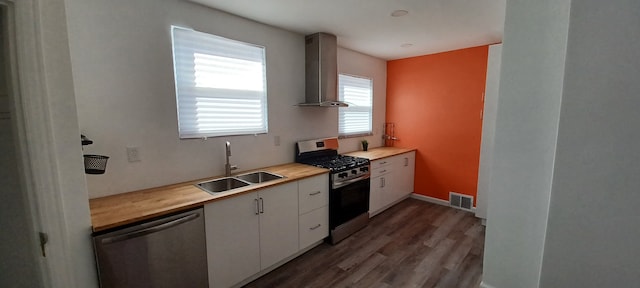 kitchen featuring white cabinetry, sink, wall chimney exhaust hood, stainless steel appliances, and wooden counters