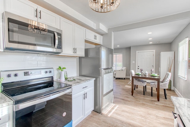 kitchen featuring light stone counters, light wood-type flooring, a notable chandelier, stainless steel appliances, and white cabinets