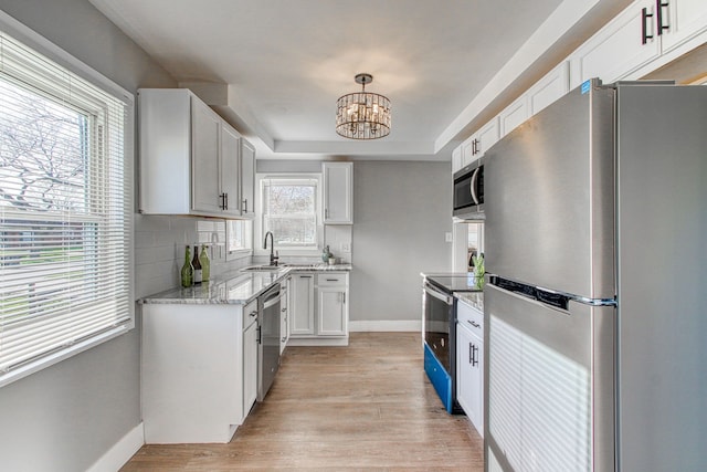 kitchen featuring appliances with stainless steel finishes, pendant lighting, sink, white cabinets, and light hardwood / wood-style floors