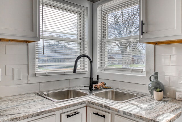 kitchen featuring white cabinetry, sink, light stone counters, and backsplash