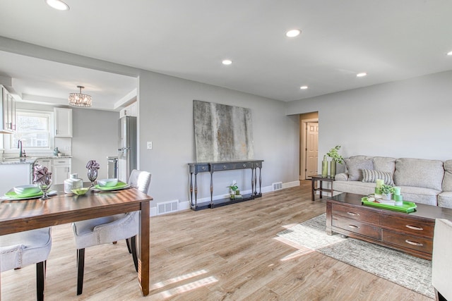 living room featuring an inviting chandelier, sink, and light hardwood / wood-style floors