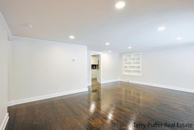 empty room featuring dark hardwood / wood-style floors, built in features, and ornamental molding