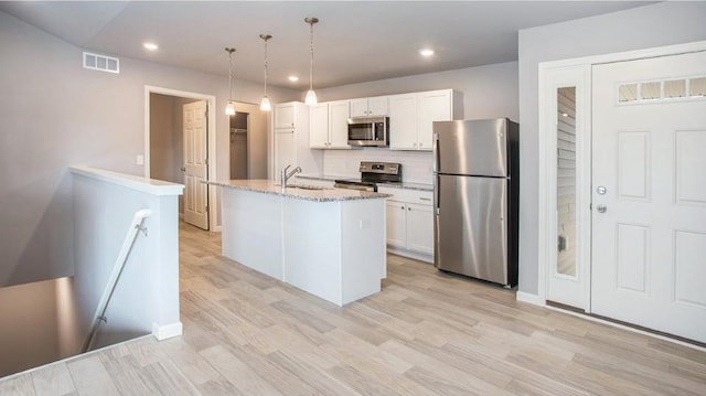 kitchen with an island with sink, appliances with stainless steel finishes, white cabinets, and hanging light fixtures