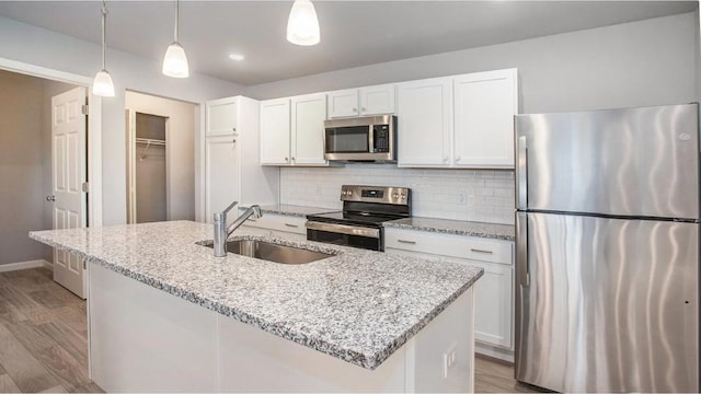 kitchen featuring stainless steel appliances, sink, white cabinets, pendant lighting, and a kitchen island with sink