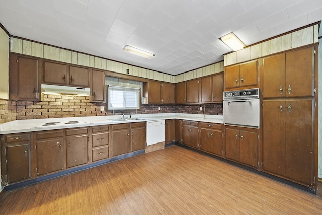 kitchen with decorative backsplash, light wood-type flooring, white appliances, and sink