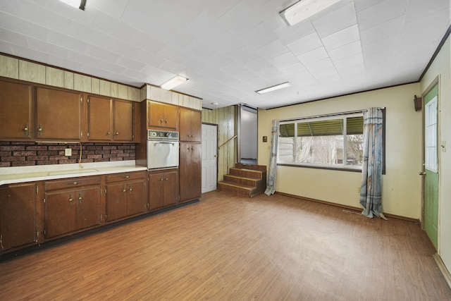 kitchen with wall oven, tasteful backsplash, ornamental molding, and light wood-type flooring