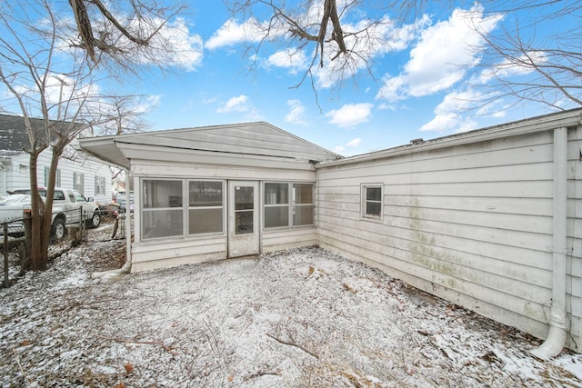 snow covered rear of property with a sunroom