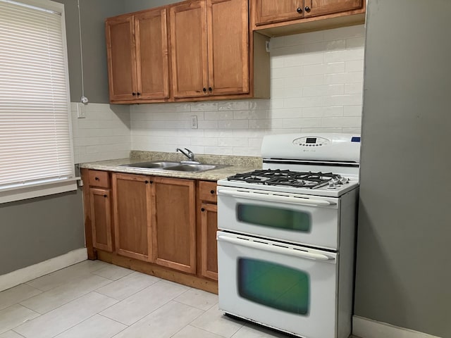 kitchen featuring decorative backsplash, light tile patterned flooring, white range with gas stovetop, and sink