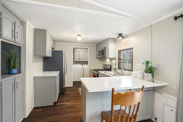 kitchen with kitchen peninsula, appliances with stainless steel finishes, a kitchen breakfast bar, sink, and separate washer and dryer