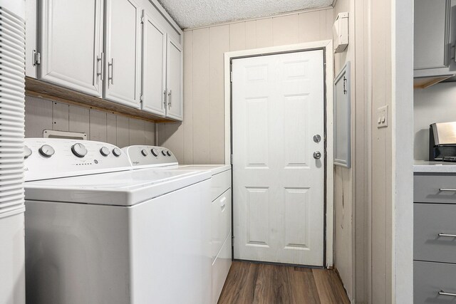 laundry area with dark wood-type flooring, cabinets, washing machine and dryer, wood walls, and a textured ceiling