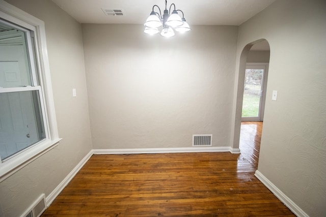 empty room with dark wood-type flooring and an inviting chandelier