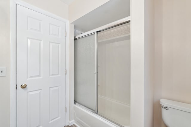 bathroom featuring toilet and bath / shower combo with glass door