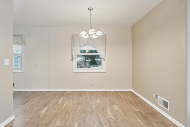 spare room featuring a notable chandelier and light wood-type flooring