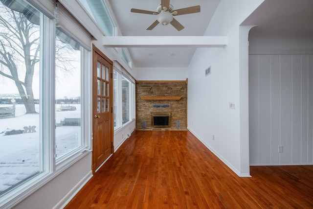 unfurnished living room featuring ceiling fan, a stone fireplace, dark wood-type flooring, and plenty of natural light