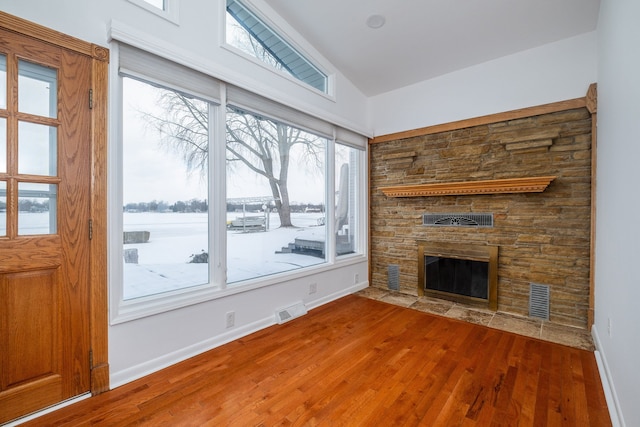 unfurnished living room with a wealth of natural light, hardwood / wood-style floors, lofted ceiling, and a stone fireplace