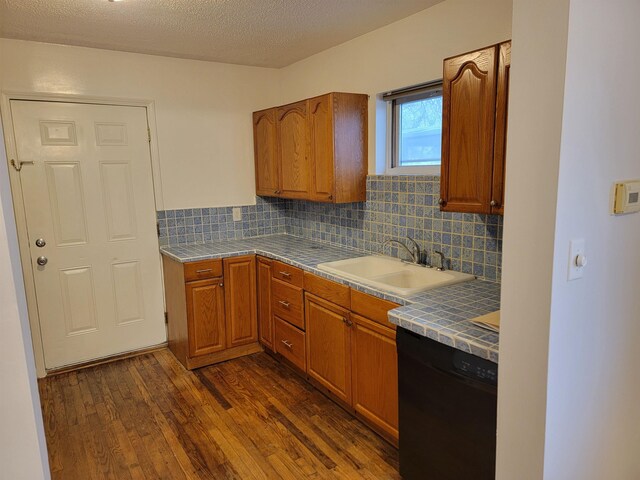 kitchen with sink, a textured ceiling, black dishwasher, tasteful backsplash, and dark hardwood / wood-style flooring