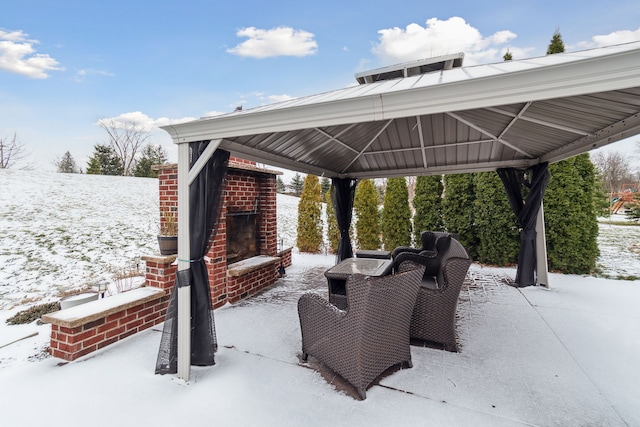 snow covered patio with a gazebo and an outdoor brick fireplace