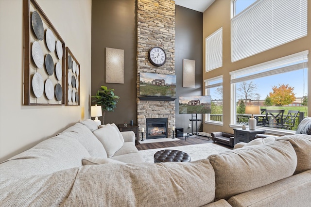 living room with a stone fireplace, hardwood / wood-style floors, a towering ceiling, and a healthy amount of sunlight