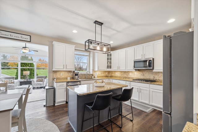 kitchen with white cabinetry, hanging light fixtures, stainless steel appliances, light stone counters, and a kitchen island