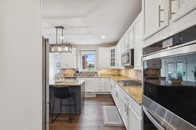 kitchen featuring appliances with stainless steel finishes, backsplash, light stone counters, white cabinets, and hanging light fixtures