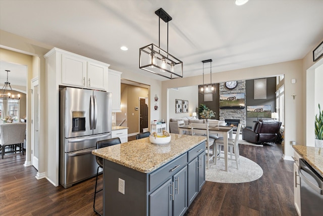 kitchen featuring pendant lighting, a stone fireplace, appliances with stainless steel finishes, a kitchen island, and white cabinetry