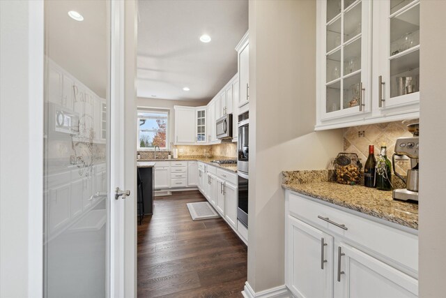 kitchen featuring appliances with stainless steel finishes, light stone counters, sink, dark hardwood / wood-style floors, and white cabinetry