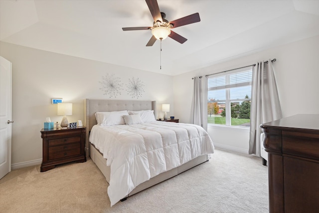 bedroom featuring a raised ceiling, ceiling fan, and light carpet