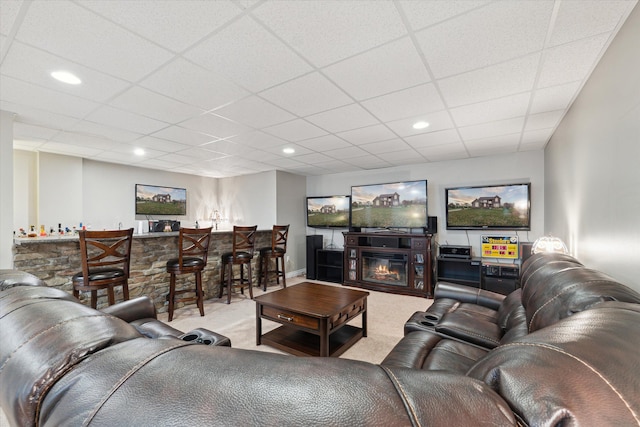 carpeted living room featuring a paneled ceiling, a stone fireplace, and indoor bar