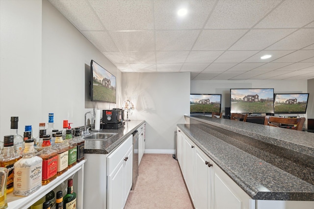 kitchen featuring a paneled ceiling, white cabinets, sink, stainless steel dishwasher, and light colored carpet