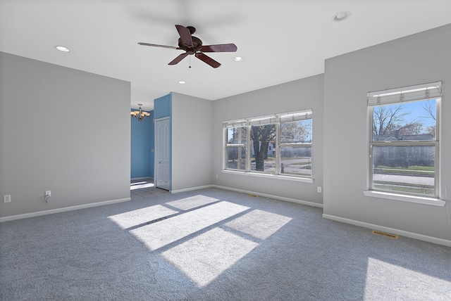 carpeted spare room with ceiling fan with notable chandelier and a wealth of natural light