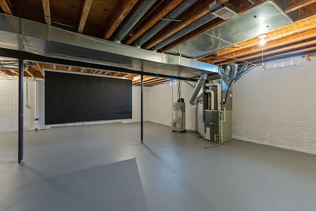 basement featuring gas water heater, brick wall, and heating unit